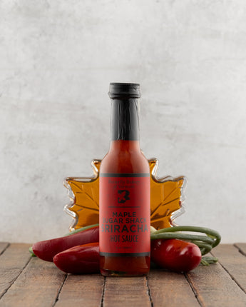Bottle of hot sauce with a red label on a wooden surface with vegetables and a leaf decoration.