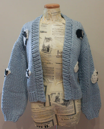 Blue knitted cardigan with pom-pom details on a mannequin against a plain background