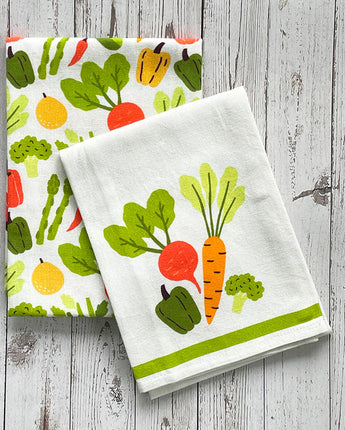 Two kitchen towels with vegetable patterns on a wooden surface