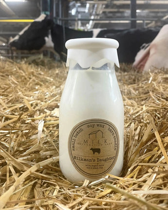 Bottle of 'Milkmaker's Daughter' soy wax candle on hay with cows in the background