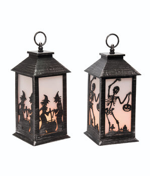 Two plastic lanterns with Halloween-themed designs, one featuring silhouettes of witches and the other of a skeleton, against a dark background.