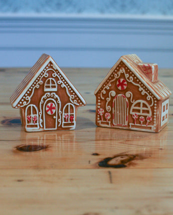 Two miniature gingerbread house salt and pepper shakers on a wooden surface with a blurred background.
