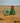 Two decorative items on a wooden surface: a green flower-shaped object and a small green tree with a red bow.