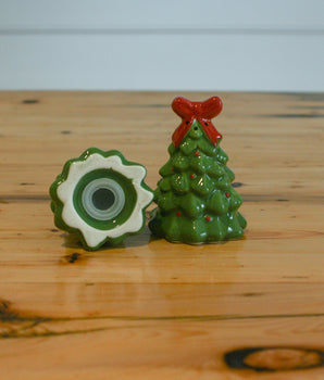 Two decorative items on a wooden surface: a green flower-shaped object and a small green tree with a red bow.