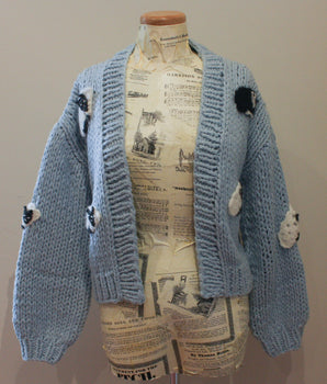 Blue knitted cardigan with pom-pom details on a mannequin against a plain background