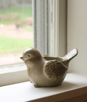 Ceramic bird-shaped planter on a windowsill with a blurred outdoor background