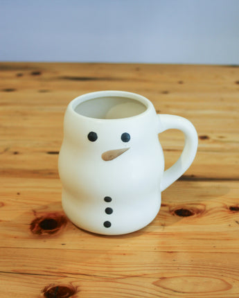 White snowman-shaped mug on a wooden surface with a plain background