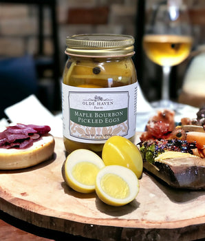 Jar of Olde Haven Farm Maple Bourbon Pickled Eggs on a charcuterie board with sliced eggs and cured meats.