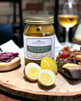 Jar of Olde Haven Farm Maple Bourbon Pickled Eggs on a charcuterie board with sliced eggs and cured meats.